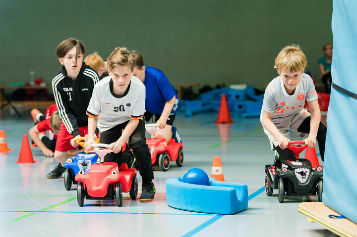 Schüler fahren auf Bobbycars während des Gaming analog Moduls im Ahorn-Sportparks