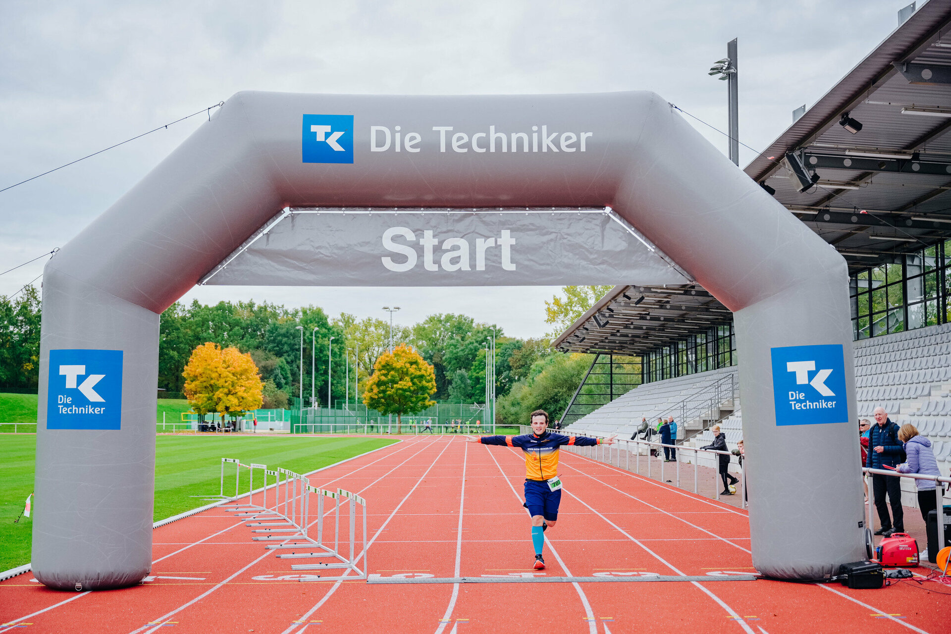 Der Zieleinlaufbogen steht auf der Tartanbahn des Leichtathletiksatdion des Ahorn-Sportpark. Unter ihm läuft ein Läufer über die Zielinie.