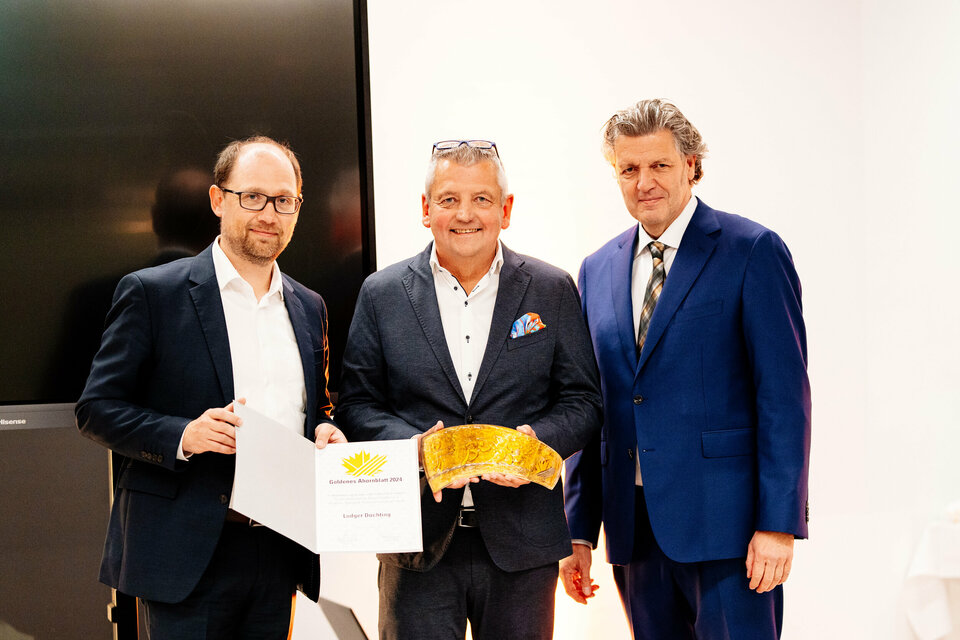 Ralf Pahlsmeier, Geschäftsfüher Ahorn-Sportpark gGmbH (stehend links), hält die Urkunde für den Preisträger des goldenen Ahornblattes. In der Mitte steht goldene Ahornblatt-Preisträger Ludger Düchting mit dem Goldenen Ahornblatt. Daneben steht Martin Nixdorf (Stiftung Westfalen, rechts im Bild).