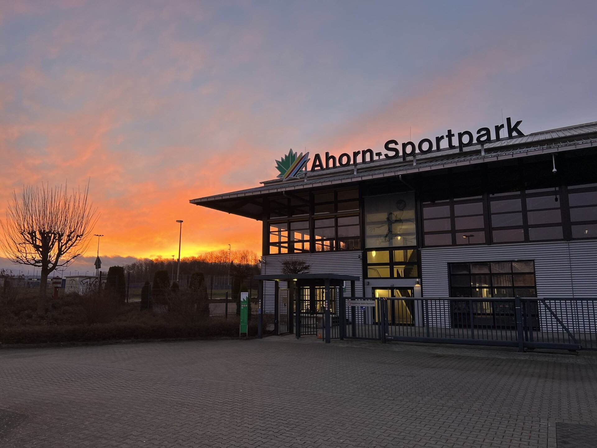 Das Bild zeigt die Nordseite der Ahorn-Sportpark-Halle im Sonnenaufgang. Hinter dem Gebäude erscheint das rötliche Licht.