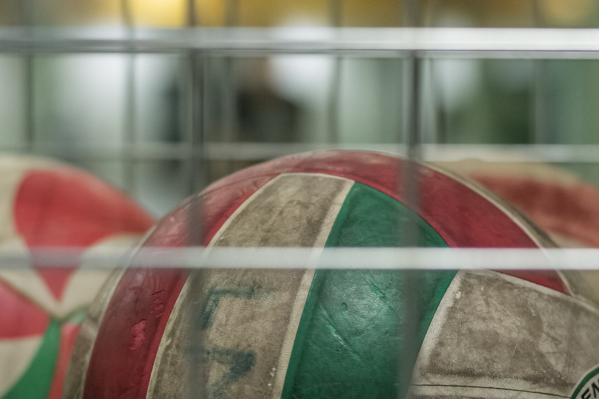 Ein rot-grün-weißer Volleyball in einem Metallgitter.