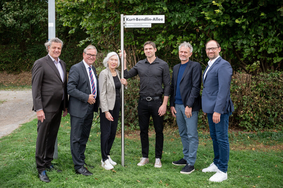 Eine Gruppe von sechs Personen steht im Ahorn-Sportpark neben einem Straßenschild mit der Aufschrift „Kurt-Bendlin-Allee“. Gemeinsam weihen sie den neuen Straßennamen ein. Zu sehen sind (von links): Martin Nixdorf, Bürgermeister Michael Dreier, Martina Bendlin, Kolja Bendlin, Dirk Happe und Ralf Pahlsmeier.