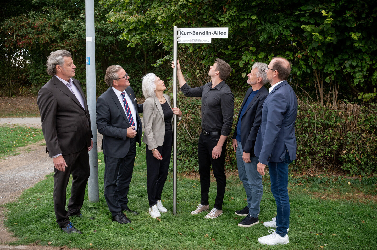 Eine Gruppe von sechs Personen steht im Ahorn-Sportpark neben einem Straßenschild mit der Aufschrift „Kurt-Bendlin-Allee“ und schauen das Schild an. Gemeinsam weihen sie den neuen Straßennamen ein. Zu sehen sind (von links): Martin Nixdorf, Bürgermeister Michael Dreier, Martina Bendlin, Kolja Bendlin, Dirk Happe und Ralf Pahlsmeier.