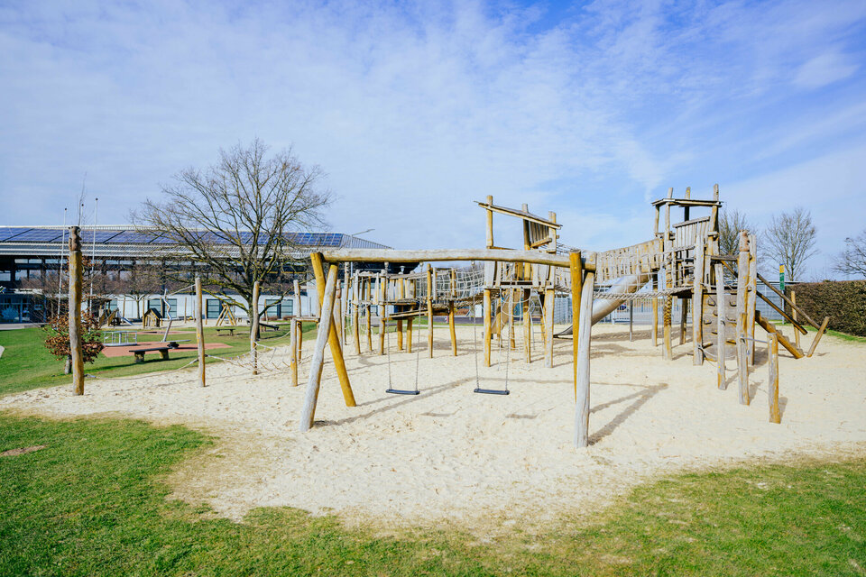 Der Spielplatz im Ahorn-Sportpark mit einem großen Klettergerüst, einer Schaukel und einem Kleinkinderspielbereich auf Sand.